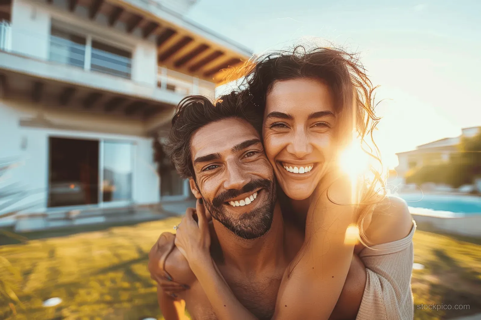 Smiling young couple piggybacking outdoors near modern homes in golden sunlight.