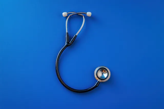 A black stethoscope with silver chest piece lies on a bright blue background for a medical health check.