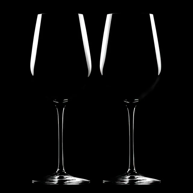 Two empty wine glasses on a black background with faint reflections on their clear stems.