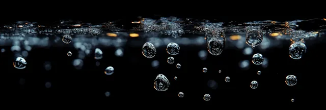 Close-up air bubbles rising in dark water with sparkling highlights and rippled surface