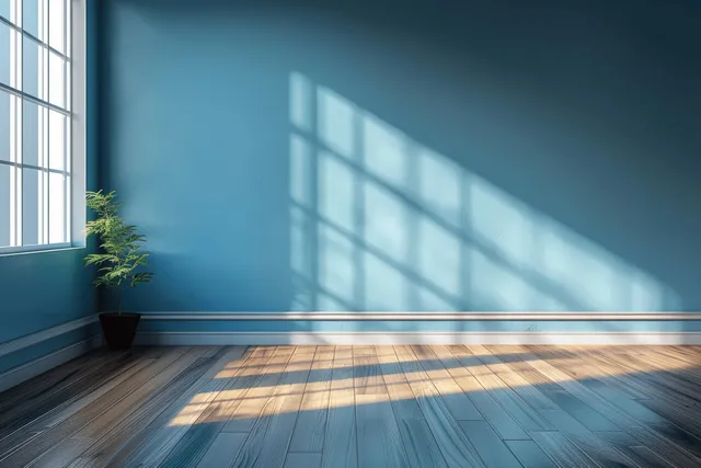 Minimal empty room with blue wall and wooden floor lit by sunlight stripes through a window.