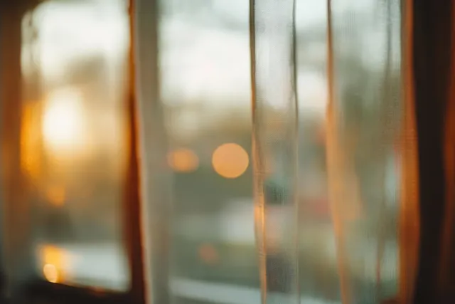 Sunlight passes through translucent curtains near a window, creating warm bokeh lights in the blurred background.