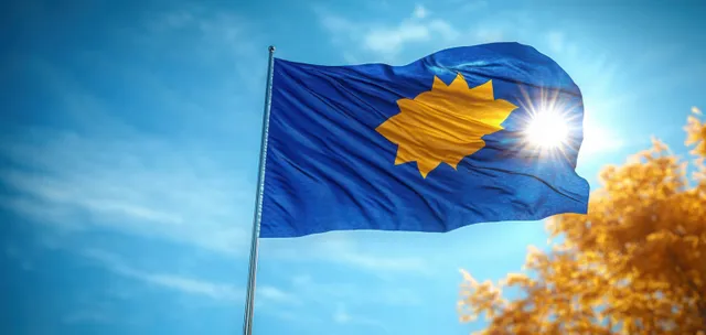 Kosovo flag waving in wind against bright blue sky with sun flare