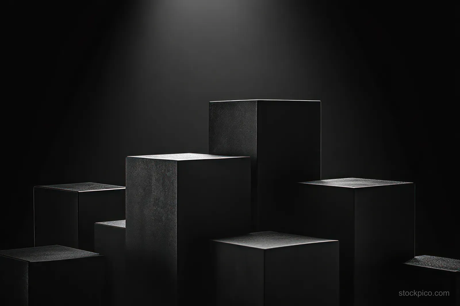 Matte black cubes stand on a dark stage under soft spotlight lighting, creating deep shadows.