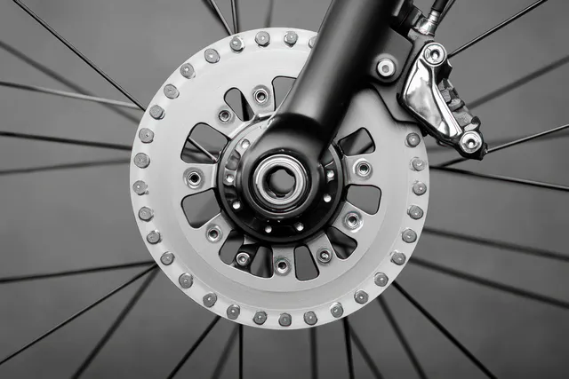 Monochrome close-up of a bicycle disc brake rotor and caliper with spokes radiating from the wheel hub.
