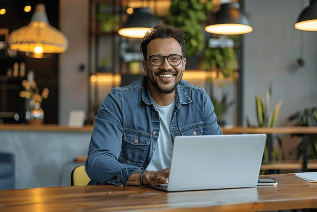 Smiling male entrepreneur on video call using laptop at desk in plant-filled modern office