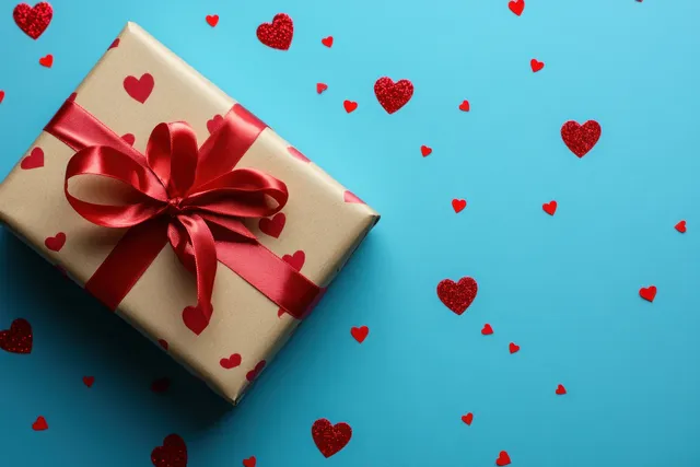 Valentine gift box with red ribbon and heart confetti on blue flat lay background