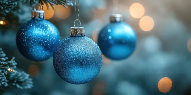 Three shiny blue Christmas ornaments hang from a branch against a soft bokeh light background with space for text.