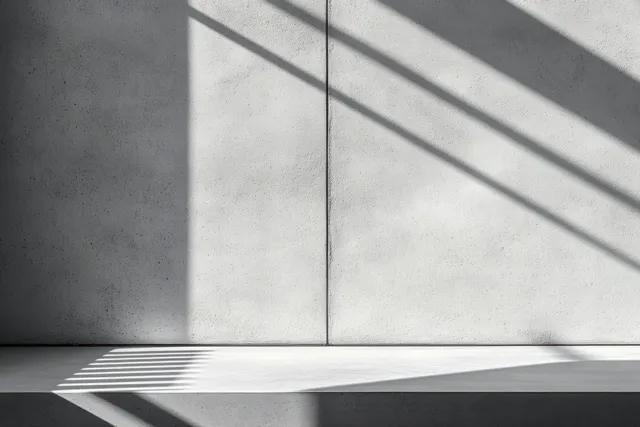 Textured concrete wall and smooth white bench with sharp geometric shadow lines from sunlight.