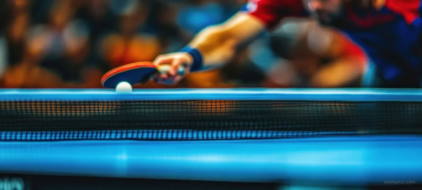 Close-up of a table tennis paddle contacting a ping pong ball over the net during an indoor match.