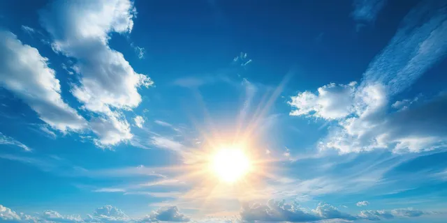 The bright sunburst in a blue sky with scattered white clouds and visible rays of light.