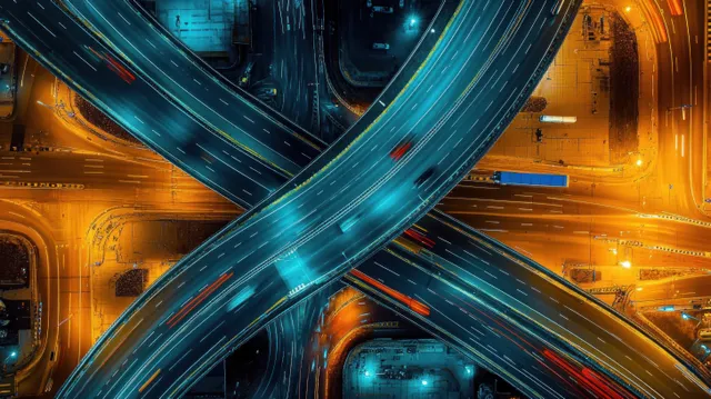 Aerial view of a lit highway interchange at night with crossing roads and vehicle light trails.