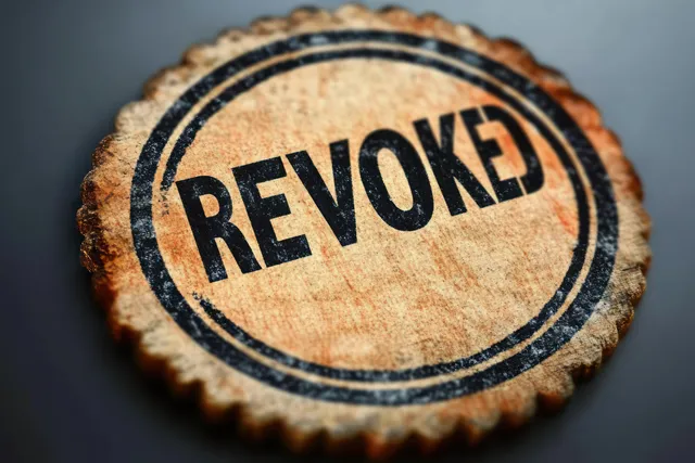 Wooden round stamp reading “REVOKED” with bold black text on stamped seal background