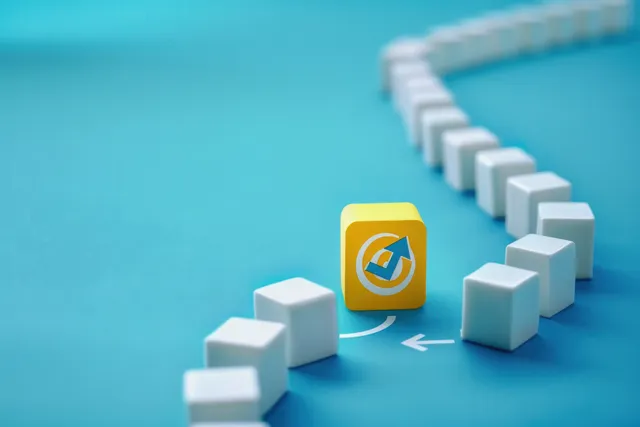 Un cubo amarillo con un emblema de flecha interrumpe una línea curva de cubos blancos sobre una superficie azul.
