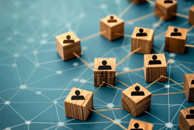 Top view of wooden cubes with people icons linked by thin lines on a blue network grid background.