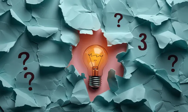 Glowing light bulb drawing emerging from torn paper with question marks above