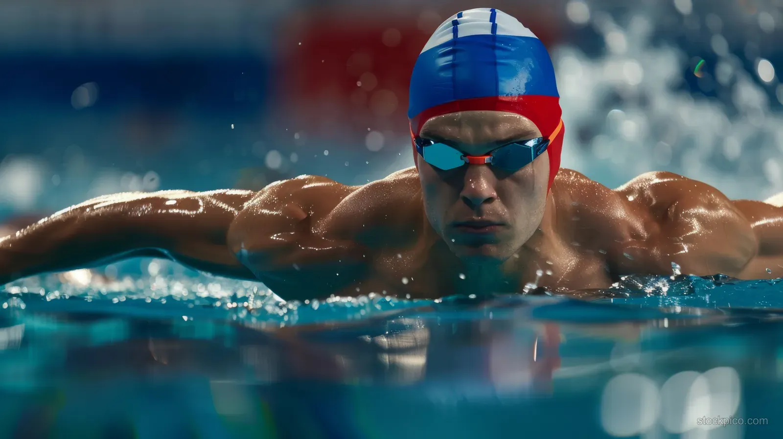 Male swimmer in breaststroke thrusting forward with splashes at the edge of a clear indoor pool.