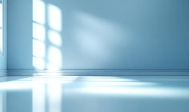 Empty pale blue room with sunlight streaming through a window onto a glossy floor.
