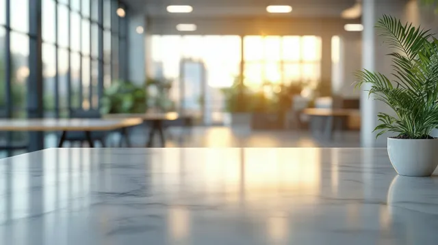 Marble office table reflects bright window light while a potted plant sits in the foreground with blurred workspace in back.