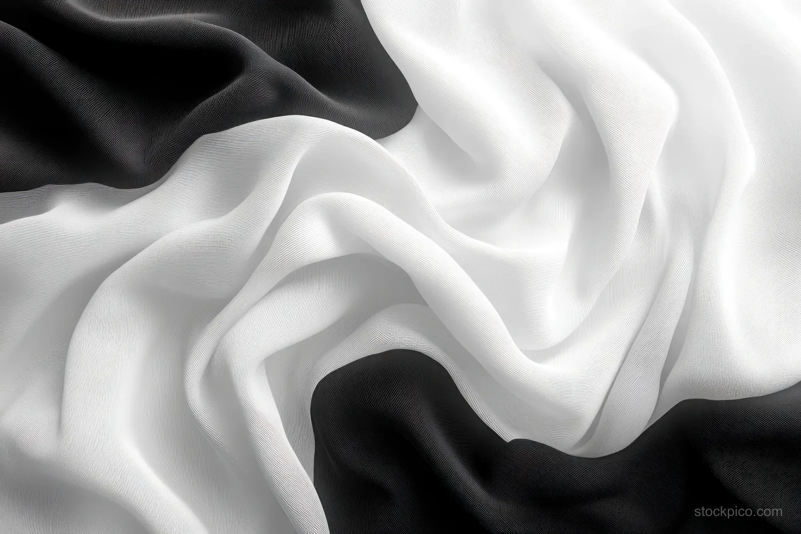 Monochrome black and white silk scarf drapes in wavy folds under soft ambient light.