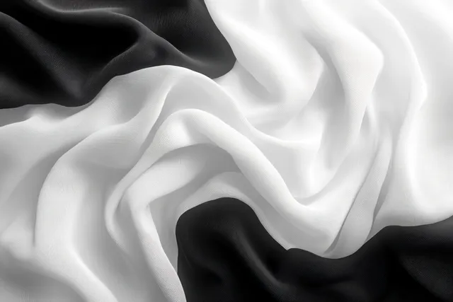 Monochrome black and white silk scarf drapes in wavy folds under soft ambient light.