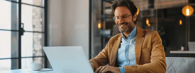 Smiling businessman typing on laptop in a modern office near a whiteboard