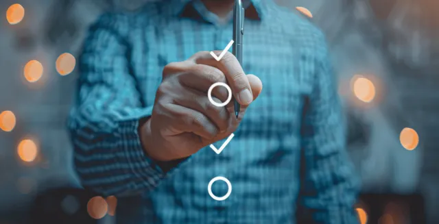 A businessman’s hand uses a pen to tick a checkmark on a quality control checklist.