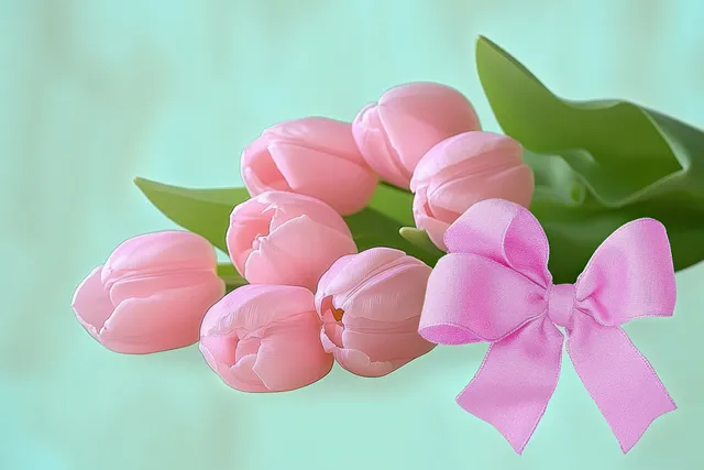 Pink tulip flowers with green leaves and a satin pink bow arranged on a soft green background.