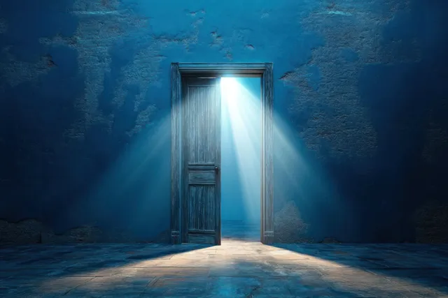 An old wooden door ajar releases bright sunbeams into a dim blue textured interior room.
