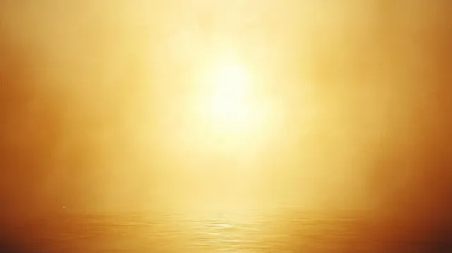 Golden sunrise glows over calm water in a misty horizon