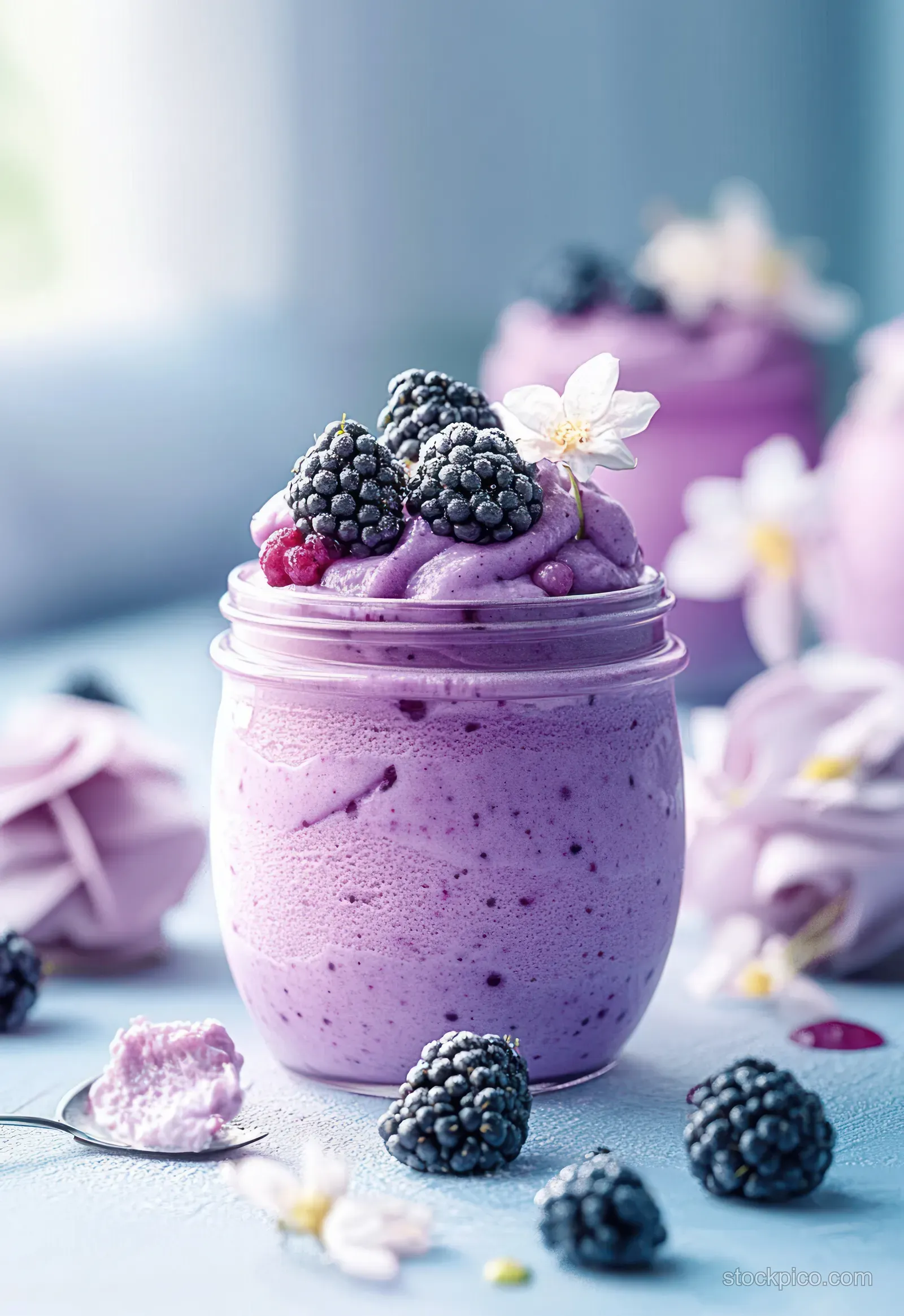 Purple blackberry mousse in a glass topped with whipped cream, blackberries, and small edible flowers.