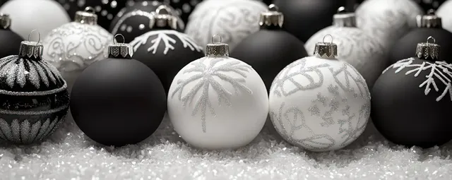 Black and white Christmas ornaments with snowflake patterns rest on glittery snow in dark light.
