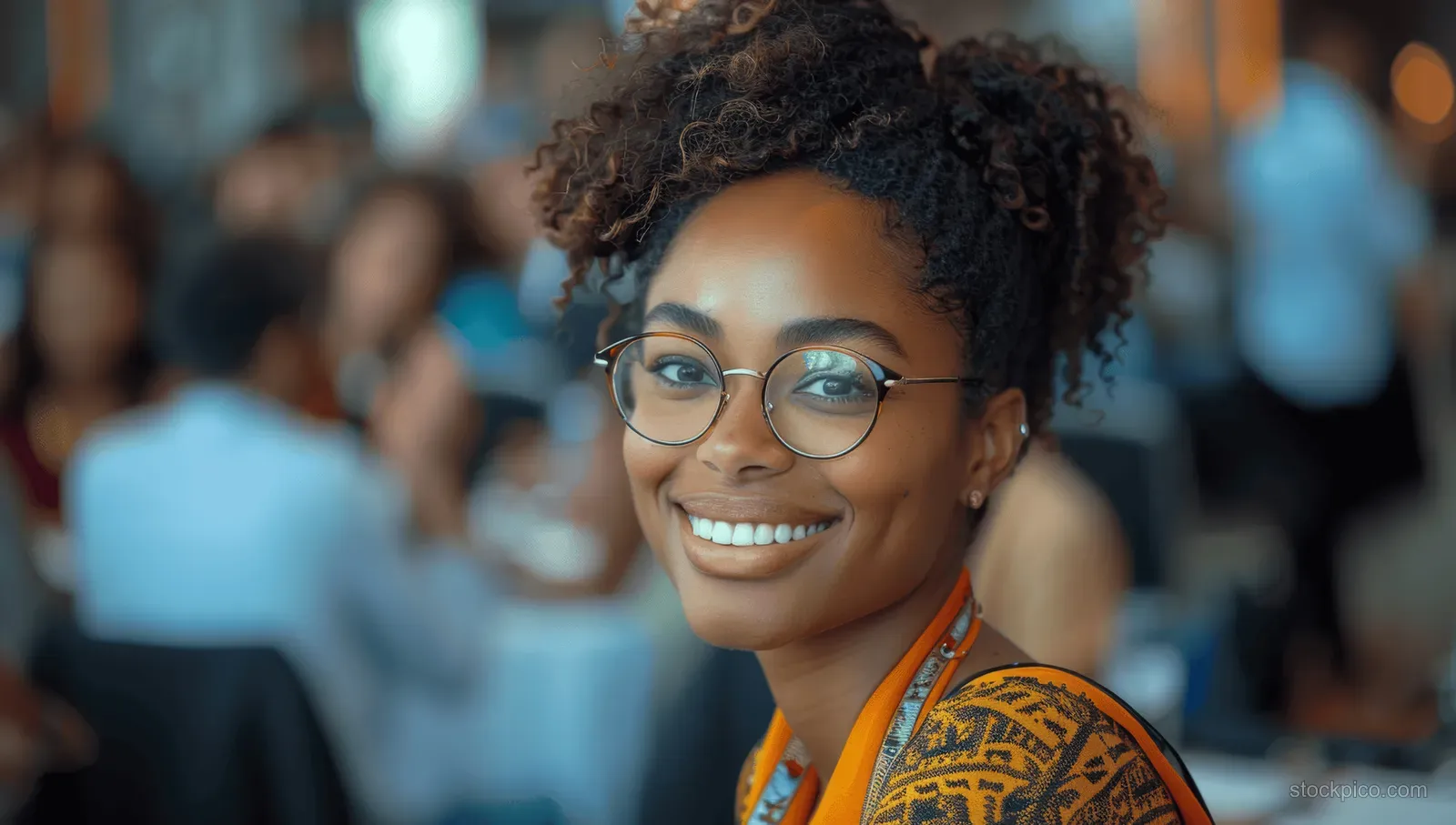 Cheerful black woman with glasses smiles at a business conference with an audience softly blurred behind her.