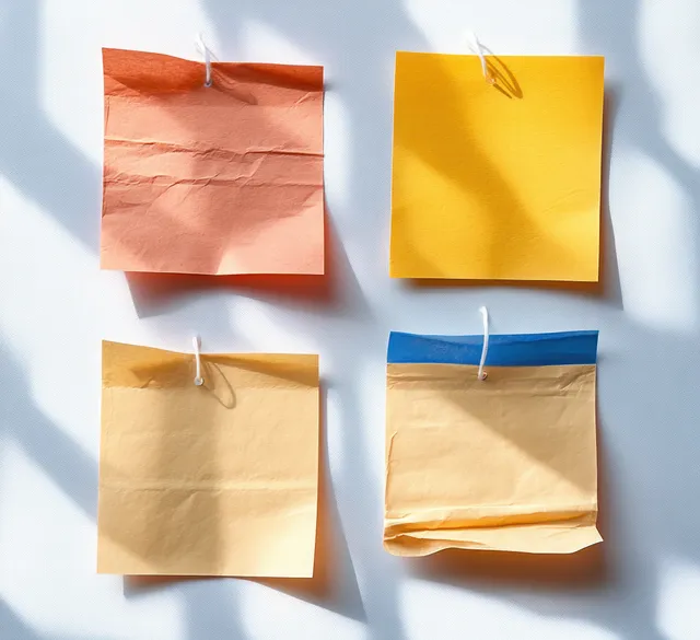 Four square sticky notes in a grid with tape fasteners casting soft shadows on a light desk surface.