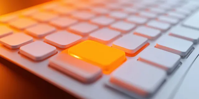 Primer plano de un teclado blanco con una tecla naranja brillante enfocada entre teclas grises.