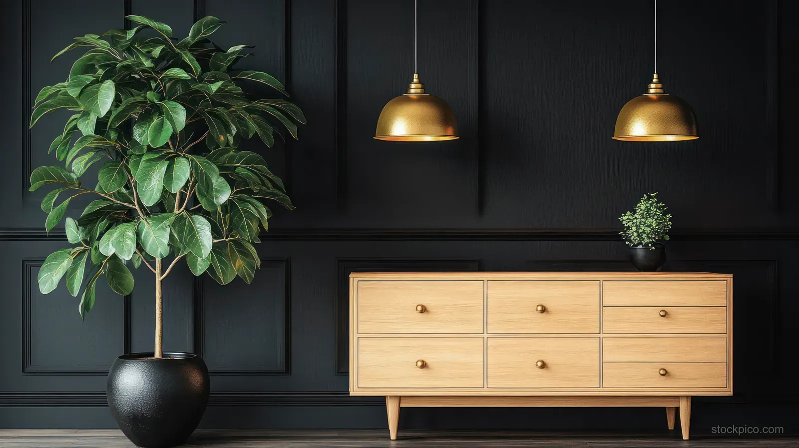 Large green potted plant beside a wooden drawer sideboard under two brass pendant lights against a dark paneled wall.