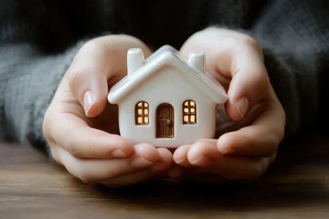 Hands holding a small house model to symbolize home protection and safety