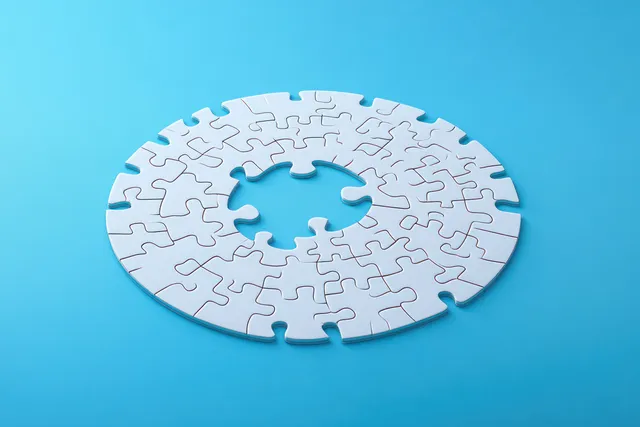 Circular white jigsaw puzzle on a bright blue background with one missing central piece.