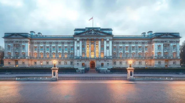 Neoclassical palace facade at dusk, featuring warm illuminated windows and intricate stone details against a cloudy sky.