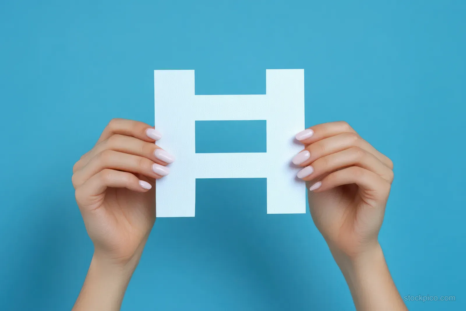 Two manicured hands hold a white cut-out letter H made of paper against a blue background.