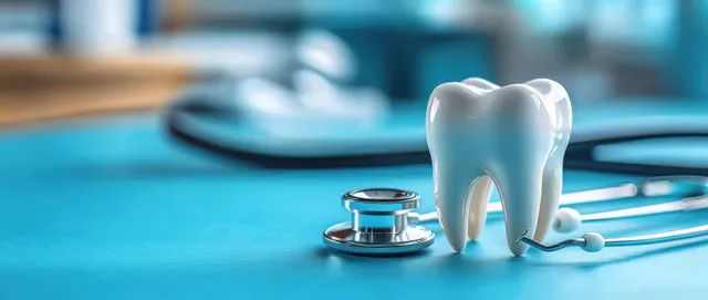 A white tooth model sits on a blue surface beside a stethoscope and dental tools.
