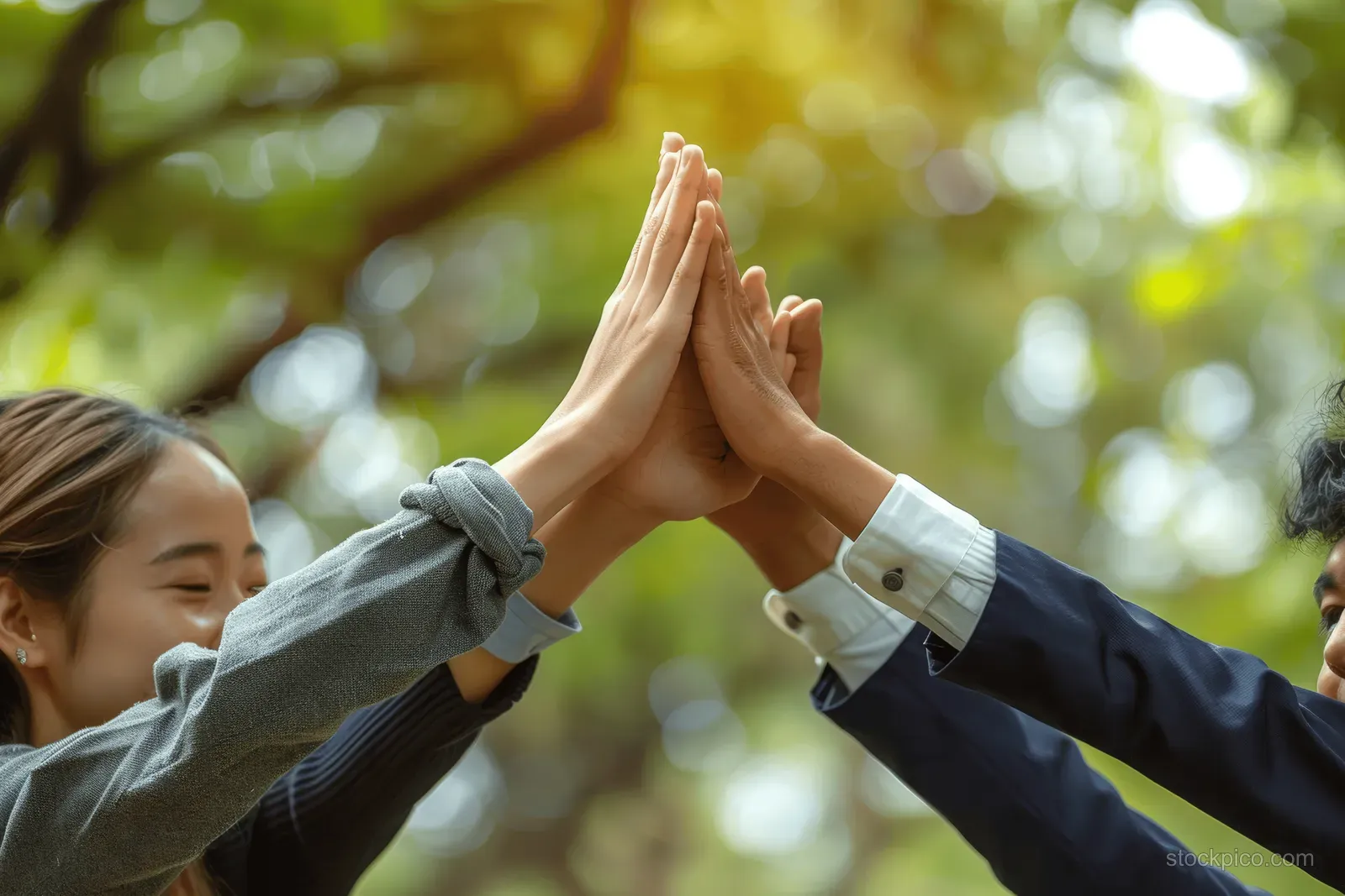 People stack their hands outdoors in a sunlit park, showing teamwork for environmental responsibility.