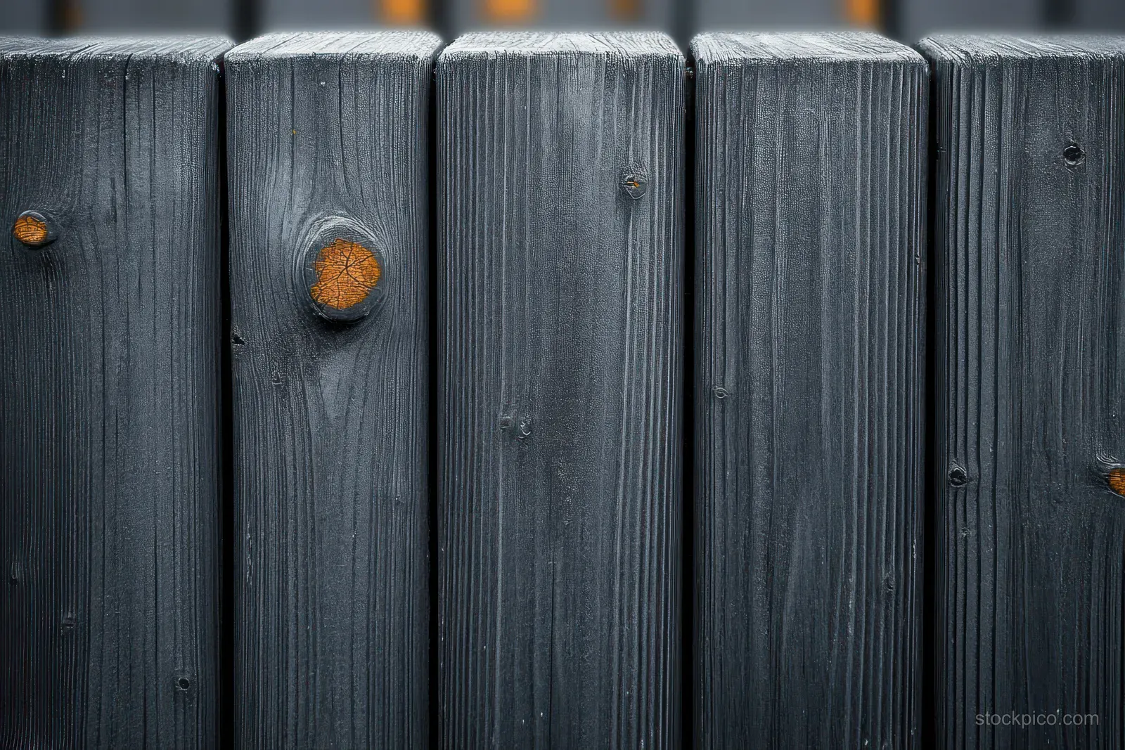 Dark charred wooden fence boards stand close together with ash stains around metal nails.