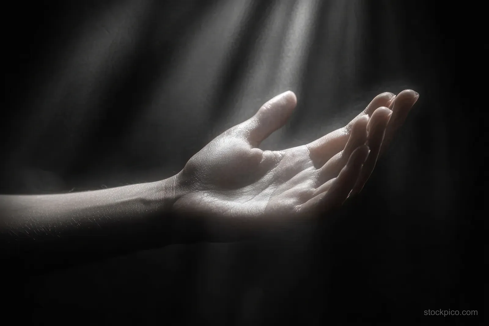 An open human hand reaches through dark space as soft light beams spill across the palm.