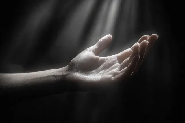 An open human hand reaches through dark space as soft light beams spill across the palm.