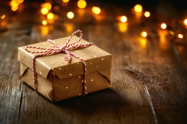 Rustic wrapped gift box on wooden table with red twine and warm bokeh lights