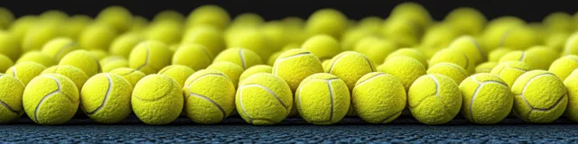 A row of bright yellow tennis balls on a court, shown in close-up with dramatic side lighting.