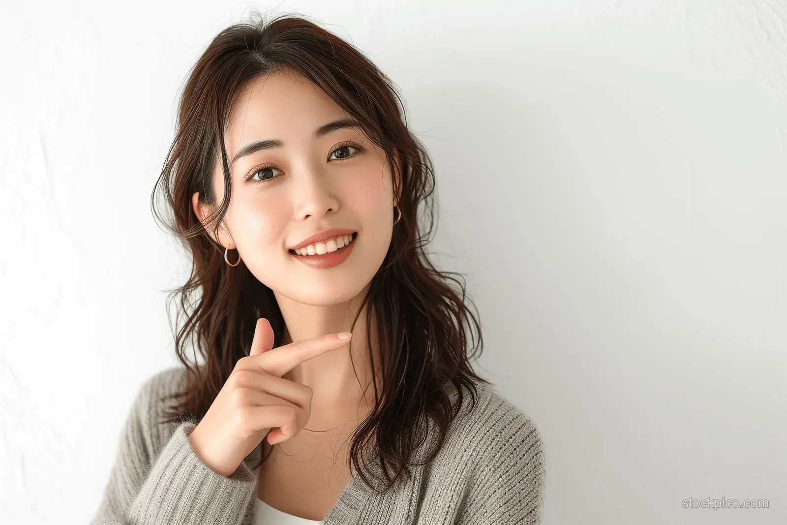 Smiling Japanese businesswoman pointing upward in a studio portrait isolated on a white background.