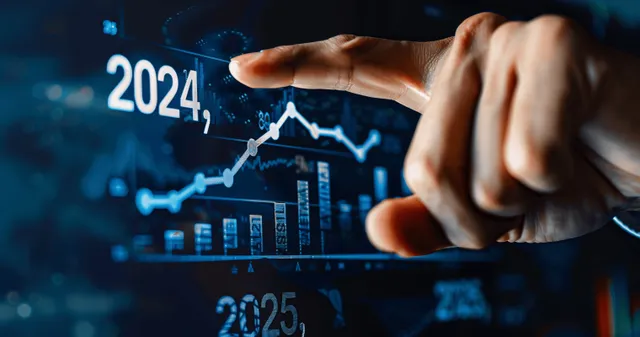A businessman points at upward line charts and numbers for 2024 and 2025 on a dark screen.