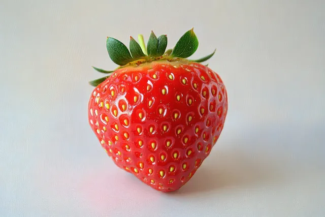 Close-up red strawberry with dew drops and green leaves on soft neutral background